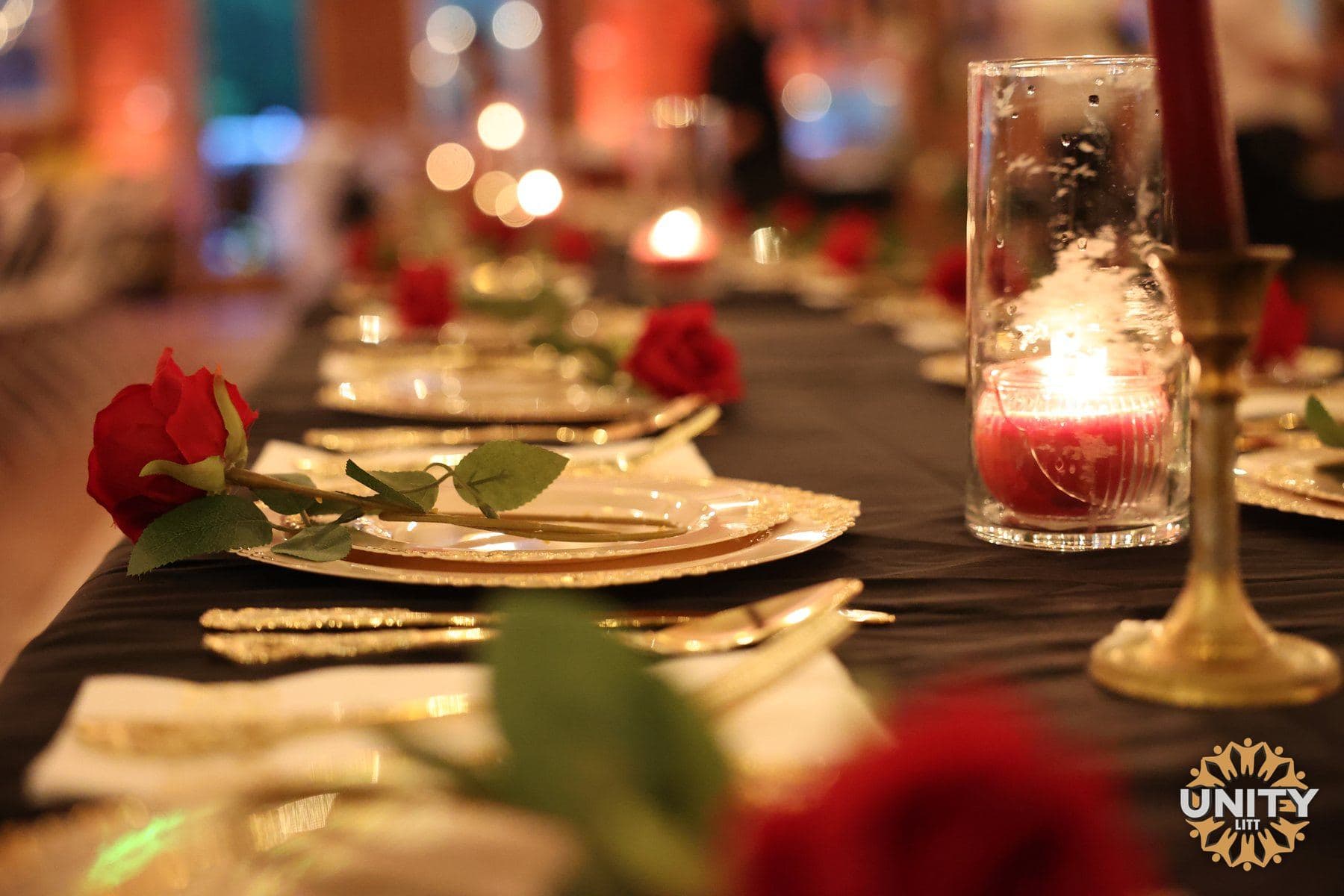 A dining table dressed with deep red roses and glassware, warm light overhead