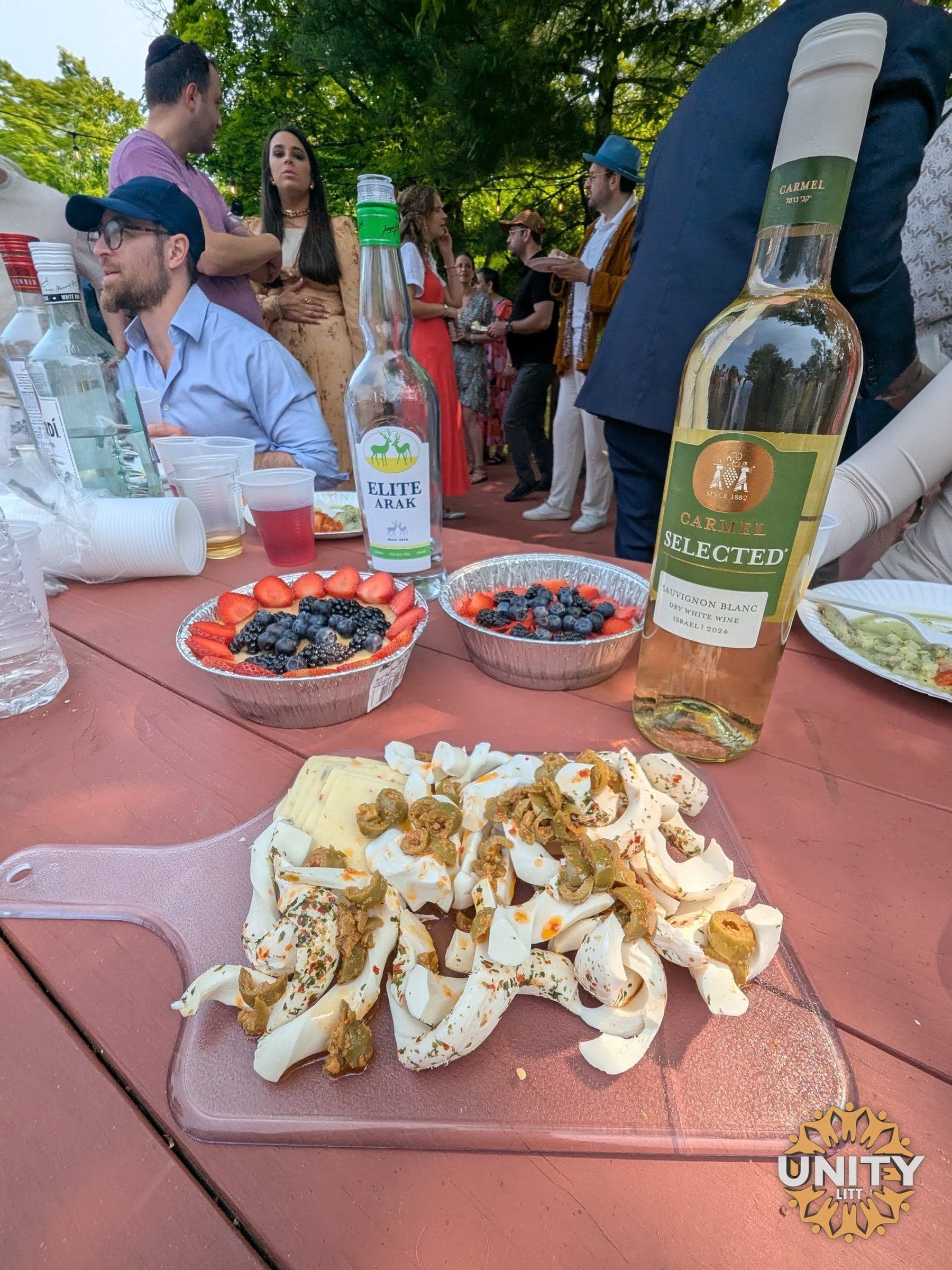 People gathered around an outdoor table, eating and talking in daylight