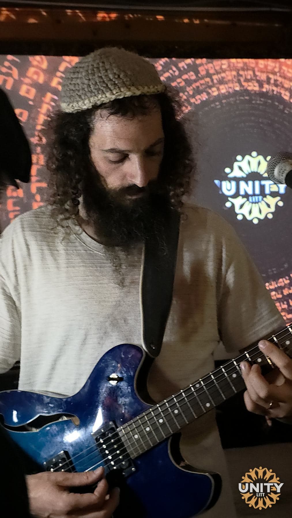 A bass player in a knitted kippah lit blue on stage