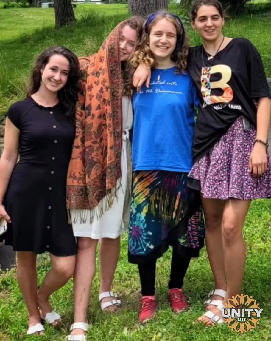 Four friends standing together on the grass, laughing