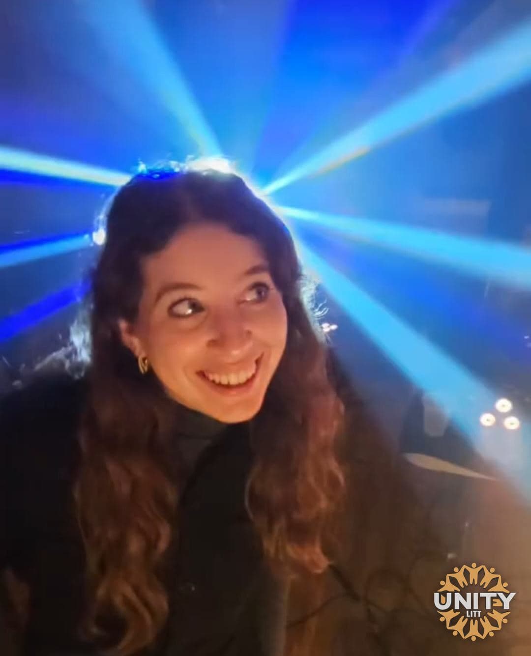 A woman laughing under blue lasers on the dance floor